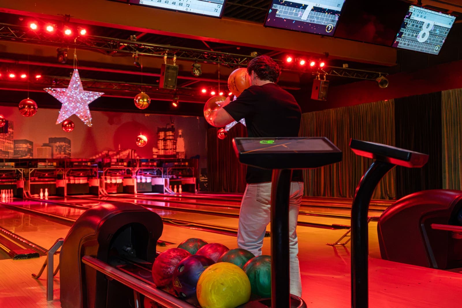 Een gast staat klaar om te gooien, met de ballen in het rek en de scoretafel in rood licht