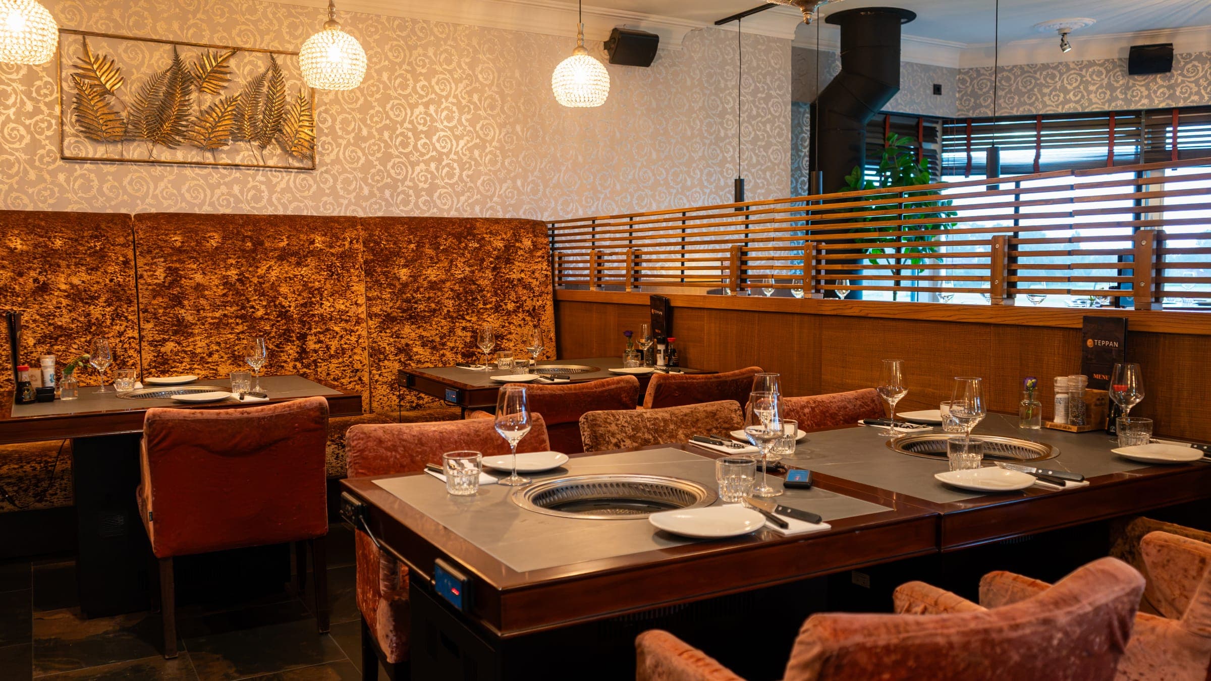 Het Teppan-restaurant van Bobs: gedekte tafels met een grillplaat in het midden, fluwelen stoelen en een lange bank