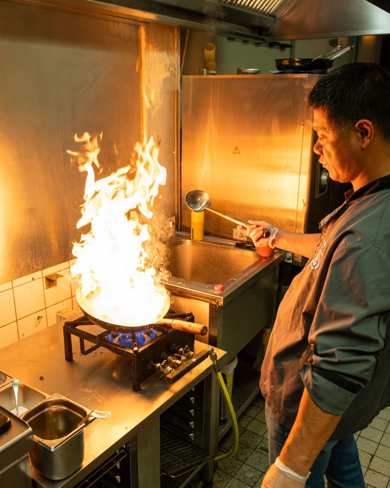 Een kok in de keuken met een wok waar de vlammen uit slaan